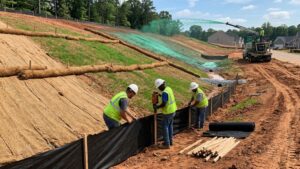 Crew installing silt fence on a hydroseeded slope at a construction site