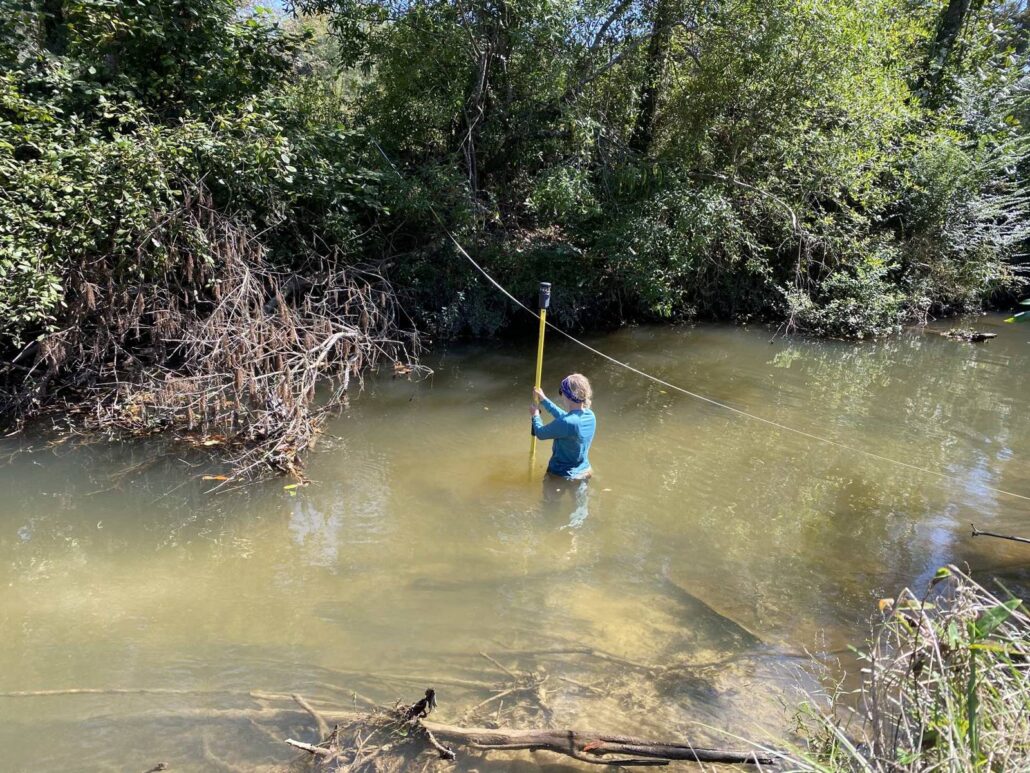 Surveyor holding a rod in a creek along a tagline to measure a stream cross section